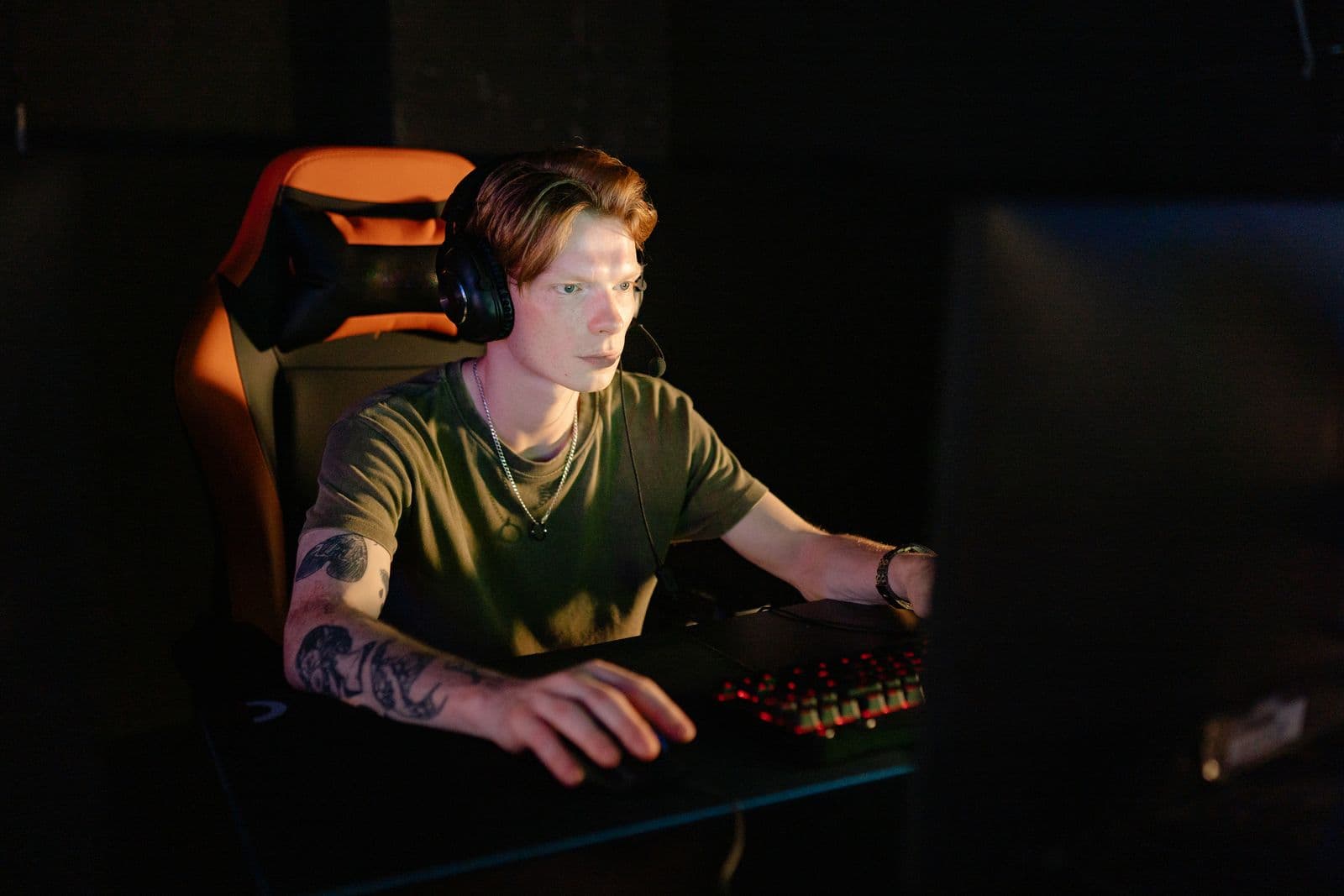 A gamer focused intently on gameplay with headphones on in a dim room