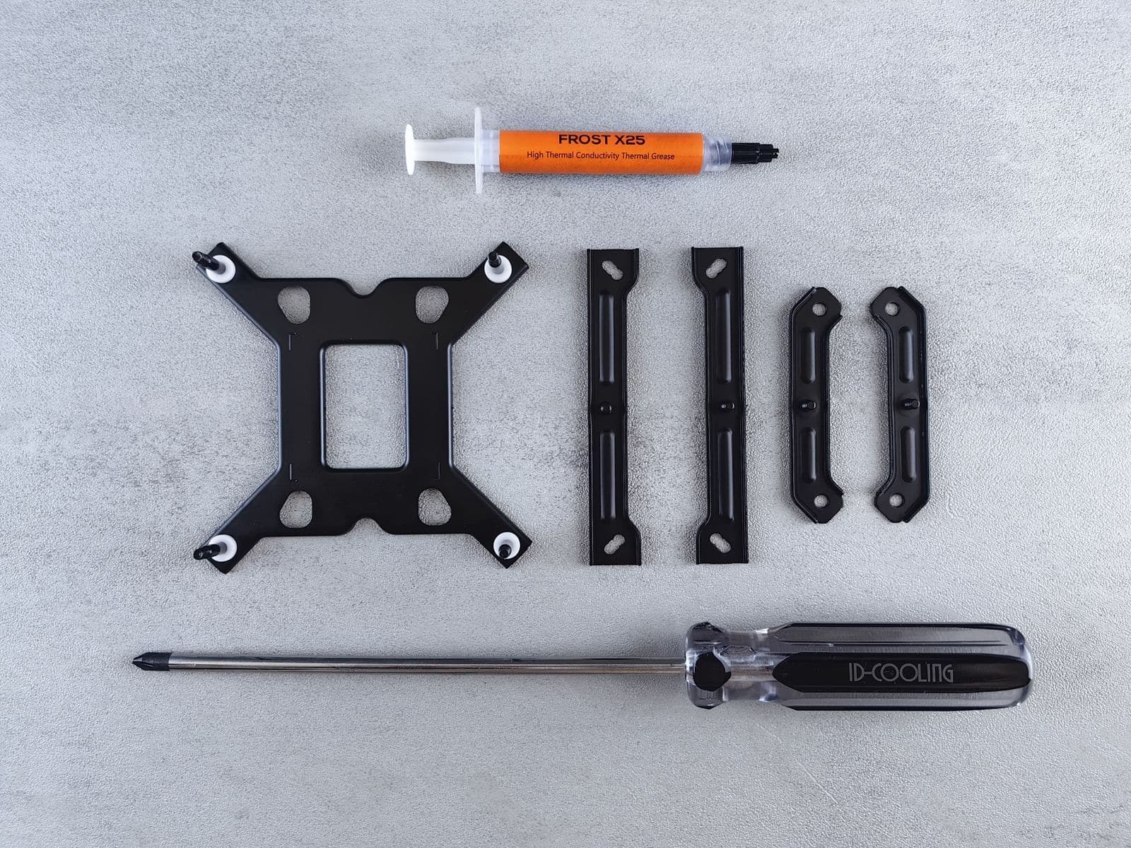 Flat lay of PC cooling kit components including thermal paste syringes, screwdrivers, and mounting hardware on a table