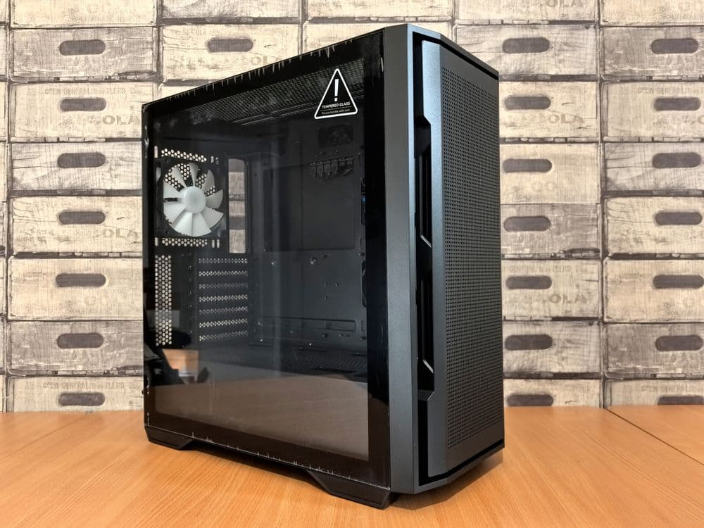 A black PC case with tempered glass side panel on a desk, revealing the interior layout including fan mounts and drive bays