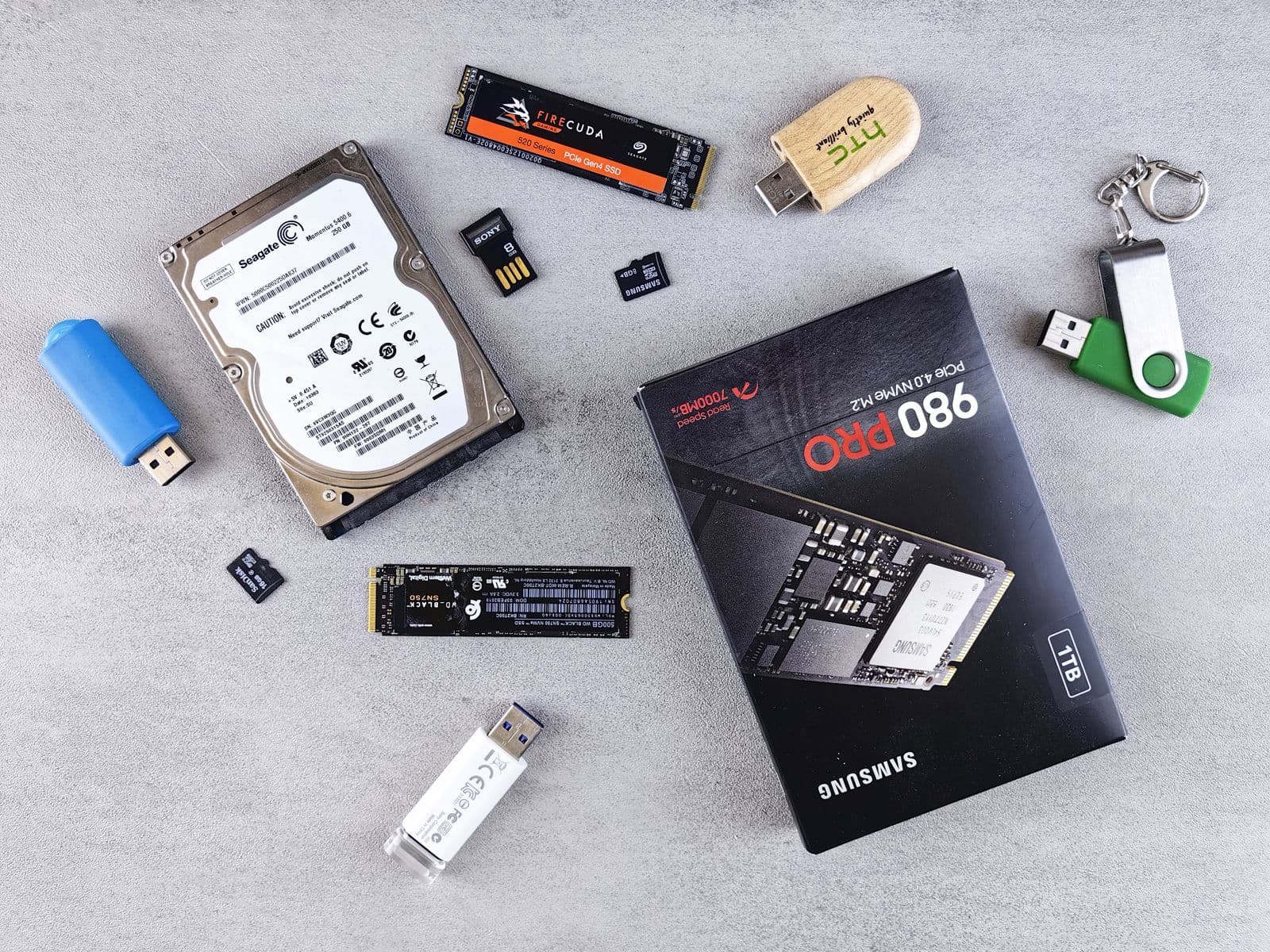 Flat lay of multiple storage drives on a desk surface showing Samsung and Seagate SATA SSDs and NVMe drives, comparing form factors for gaming PC storage options